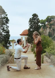 Romantic proposal at Marimurtra Garden, groom-to-be on one knee as his partner reacts with joy and surprise.