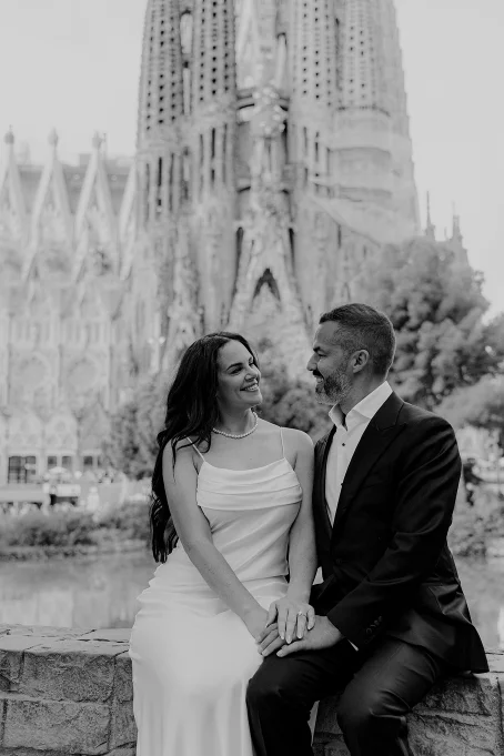 Smiling couple in elegant attire share a tender moment in front of La Sagrada Familia, Barcelona photography session.