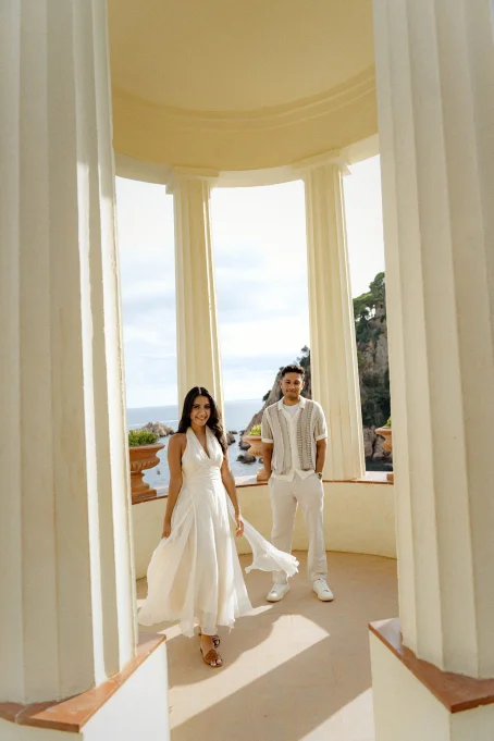Smiling couple in elegant summer outfits pose at Marimurtra garden pavilion with sea views, captured by a professional photog
