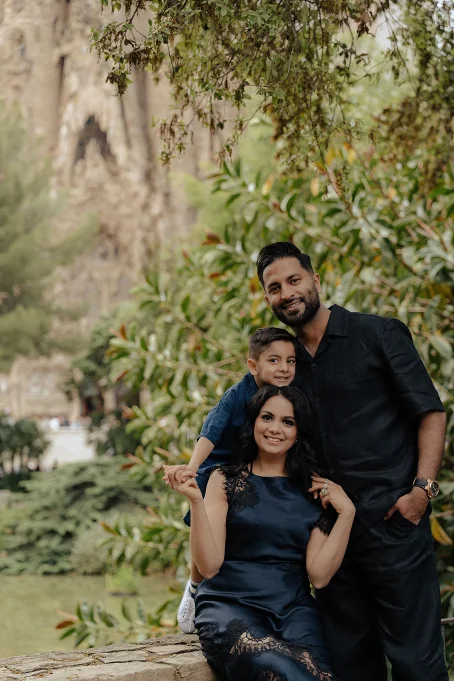 Smiling family poses together in lush gardens near La Sagrada Familia, captured by a professional photographer.