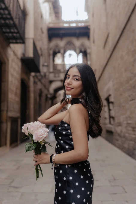 Smiling woman in a polka dot dress holding roses, captured in the charming Gothic Quarter for a portrait session.