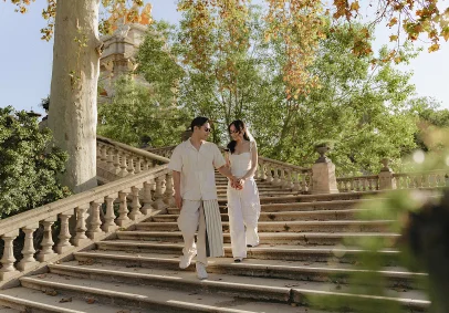 Stylish couple holding hands and smiling while walking down stone steps in Park de la Ciutadella, Barcelona.