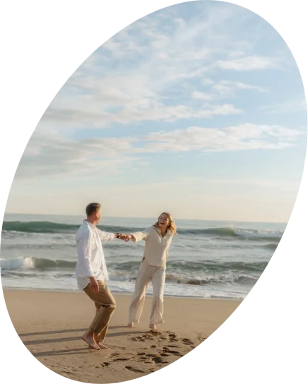Couple laughing and holding hands on a sunny Barcelona beach, captured during a relaxed Vacation Portraits photoshoot.