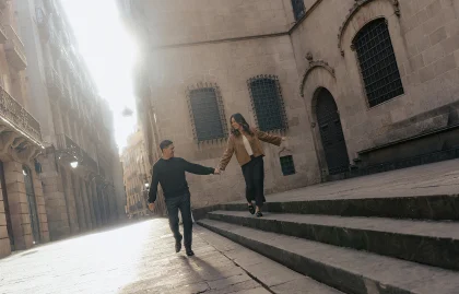 Couple holding hands and smiling during an engagement photoshoot on sunlit streets in Barcelona’s Gothic Quarter.