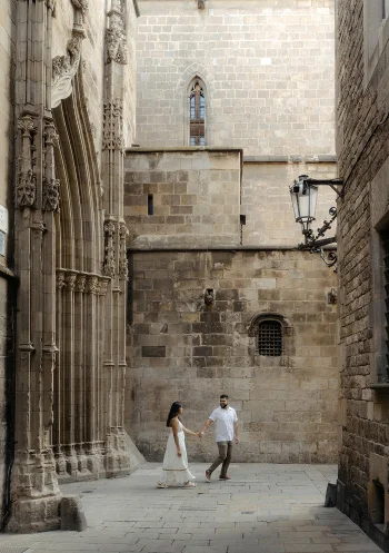 Couple holding hands and walking through a historic stone alley during a Vacation Portraits photoshoot in Barcelona.