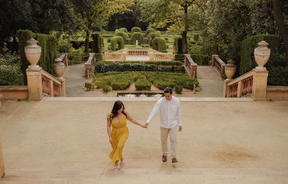Couple holding hands and walking up steps in a lush Barcelona garden during an engagement photoshoot.