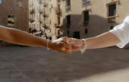 Couple holding hands during a surprise proposal photoshoot in a sunlit Barcelona square, capturing a joyful moment.