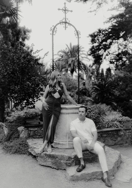 Couple poses by a stone fountain in a lush Barcelona garden, captured during a surprise proposal photoshoot.