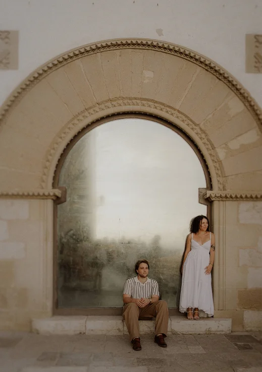 Couple sharing a quiet moment during a surprise proposal photoshoot in Barcelona, framed by a grand arched window.