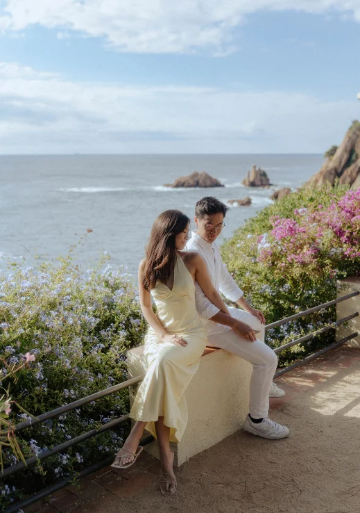 Couple sharing a tender moment during a surprise proposal photoshoot by the sea in Barcelona, surrounded by flowers.