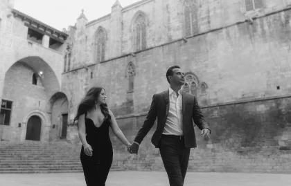 Elegant couple holding hands and walking during an engagement photoshoot in historic Barcelona.