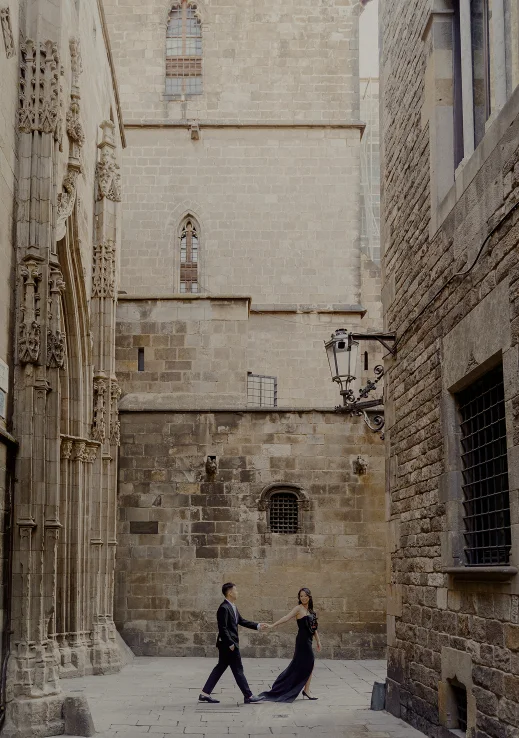 Elegant couple holding hands during an engagement photoshoot in a historic Barcelona street.