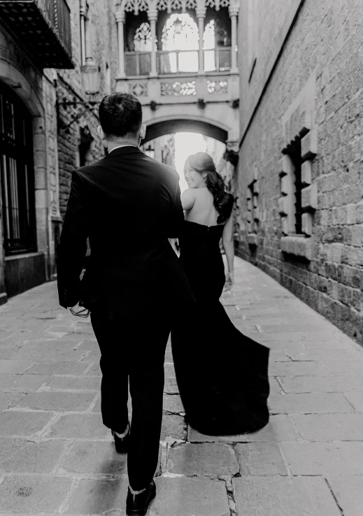 Elegant couple walking hand in hand through a historic Barcelona street, captured during an engagement photoshoot.