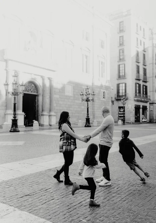 Family laughing and playing together during a Vacation Portraits photoshoot in a sunlit Barcelona square.