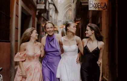 Four friends laugh and walk arm in arm during a Vacation Portraits photoshoot in a charming Barcelona street.