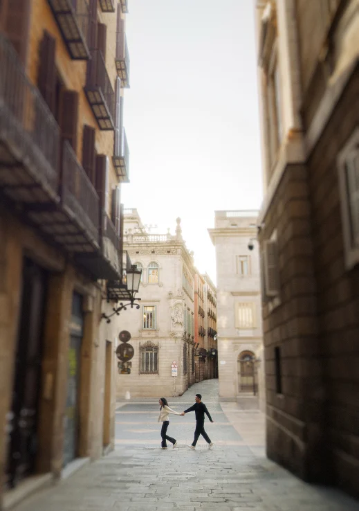Joyful couple holding hands and walking through a charming Barcelona street during an engagement photoshoot.