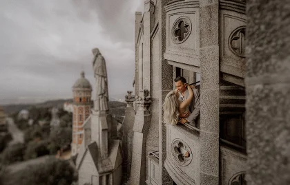 Romantic couple shares a kiss at a castle window in Barcelona, captured during an intimate engagement session.