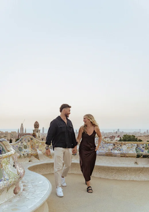 Smiling couple holding hands during a Vacation Portraits photoshoot in Park Güell, Barcelona at sunset.
