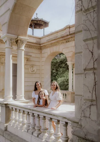 Three women smile together on a sunlit stone terrace during a Vacation Portraits photoshoot in Barcelona.
