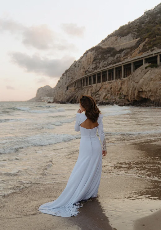 Woman in a white dress walks along the Barcelona beach at sunset, captured during a couples photoshoot session.