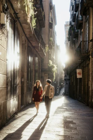 Couple holding hands and smiling as they walk through a sunlit street in Barcelona, captured for a couples photography sessio