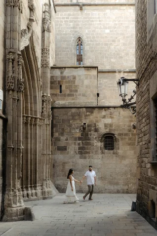 Couple holding hands and smiling during a Vacation Portraits photoshoot in a historic Barcelona alley.