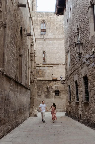 Couple holding hands and smiling while strolling through a historic alley during a Vacation Portraits photoshoot in Barcelona