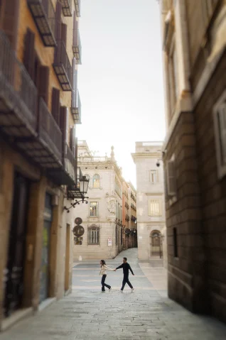 Couple holding hands and walking through a charming Barcelona street during an engagement photoshoot session.