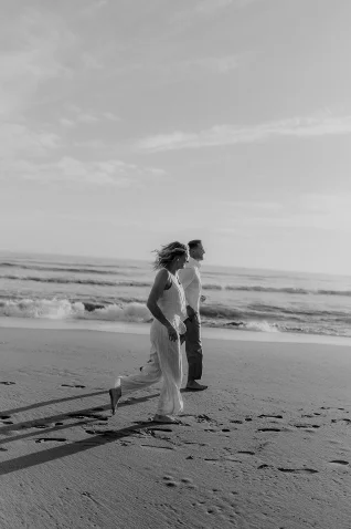Couple joyfully walking along the Barcelona beach at sunset, captured in a candid lifestyle photography session.