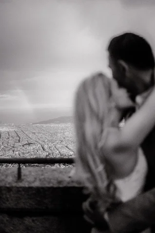 Couple shares a romantic kiss overlooking the Barcelona skyline, captured in an intimate engagement photography moment.