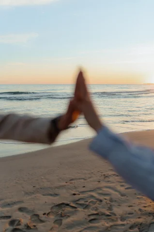 Couple sharing a joyful high five on Barcelona beach at sunset, captured during an engagement photoshoot session.