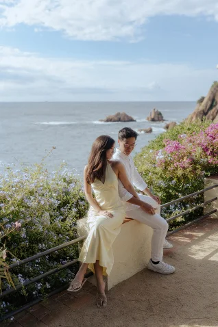 Couple sharing a joyful moment by the sea in Barcelona, surrounded by flowers, perfect for engagement photography.
