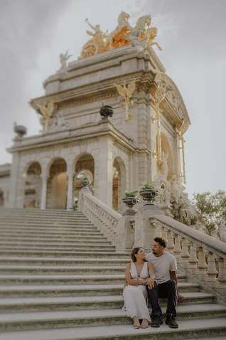 Couple sharing a joyful moment on steps at Barcelona’s iconic monument during a surprise proposal photoshoot.