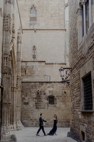 Elegant couple holding hands in a romantic photoshoot on historic Barcelona streets, perfect for engagement photography.