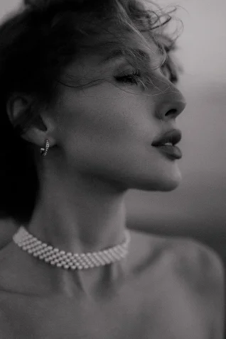 Elegant woman in Barcelona, hair tousled by the breeze, showcasing fine jewelry in a timeless portrait session.