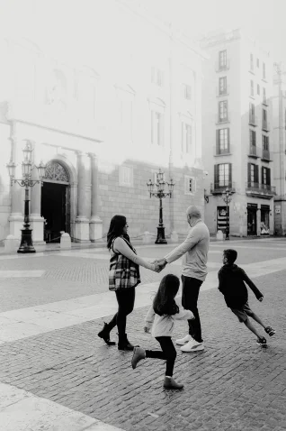 Family laughing and holding hands during a Vacation Portraits photoshoot in a sunny Barcelona square.