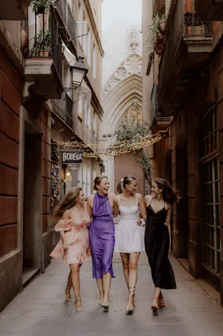 Four friends laughing and walking arm in arm during a Vacation Portraits photoshoot in a charming Barcelona street.