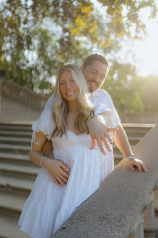 Joyful couple celebrates a surprise proposal in Barcelona, bride-to-be showing her ring on sunlit steps.