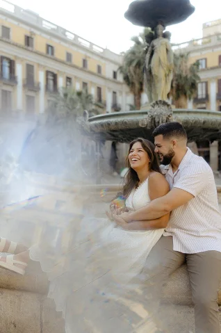Laughing couple embraces by a fountain in Barcelona during a couples & engagements photoshoot.