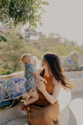 Mother and baby share a joyful moment on a mosaic bench during a Vacation Portraits photoshoot in Barcelona.