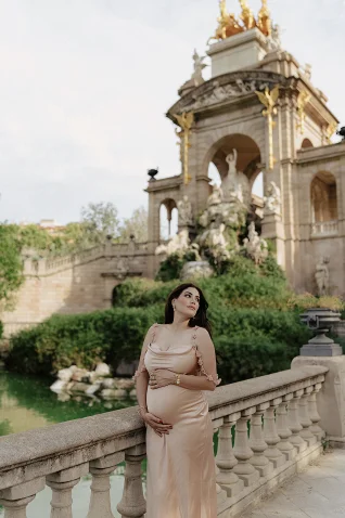 Pregnant woman in elegant dress poses by the Cascada Monumental in Barcelona during a vacation portrait photoshoot.