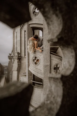 Romantic couple shares a kiss on a stone balcony in Barcelona, captured during an intimate engagement photoshoot.