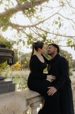 Romantic couples photoshoot in Barcelona, capturing a tender moment under leafy branches by a stone railing.