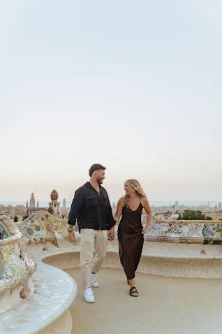 Smiling couple holding hands during a Vacation Portraits photoshoot in Park Güell, Barcelona at sunset.