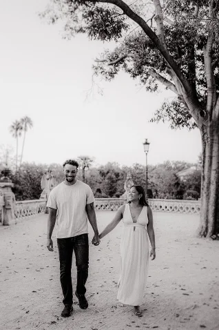 Smiling couple holding hands during an engagement photoshoot in a scenic Barcelona park.
