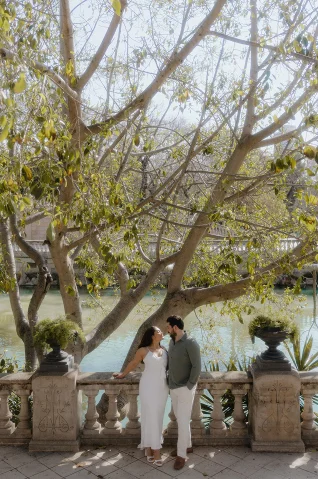 Smiling couple shares a romantic moment by a sunlit pond in Barcelona, captured during an engagement photoshoot.