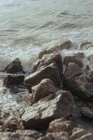 Waves gently crash over sunlit rocks on a Barcelona shore, capturing a tranquil vacation portrait scene.