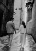 Couple holding hands and walking down a historic cobblestone street, captured during an engagement photoshoot.