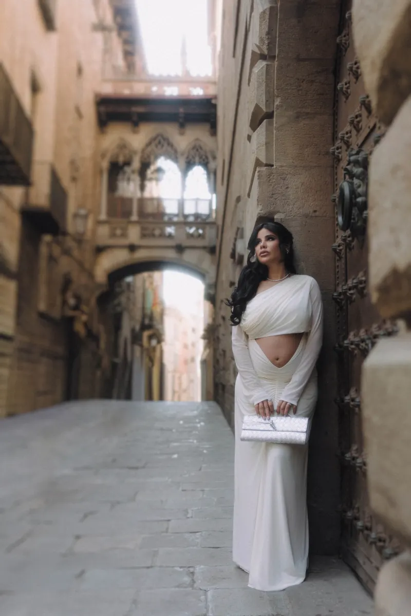 Elegant woman in a white dress poses on a charming Barcelona street during a Vacation Portraits photoshoot.