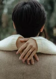 Engaged couple embracing outdoors, her hand with an engagement ring resting on his shoulder, couples photoshoot.